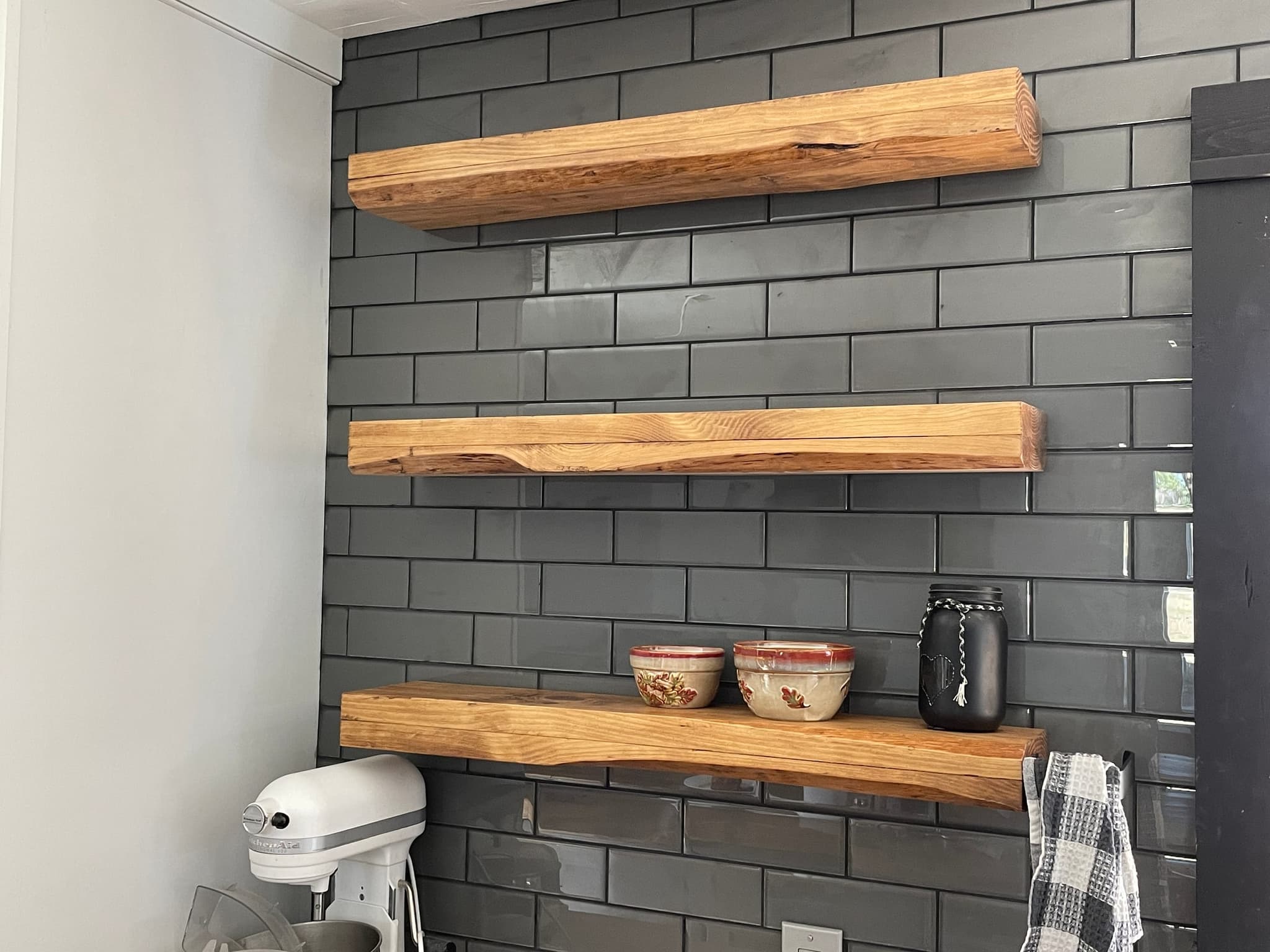 Glass tile wall with rustic floating shelves set on concealed steel