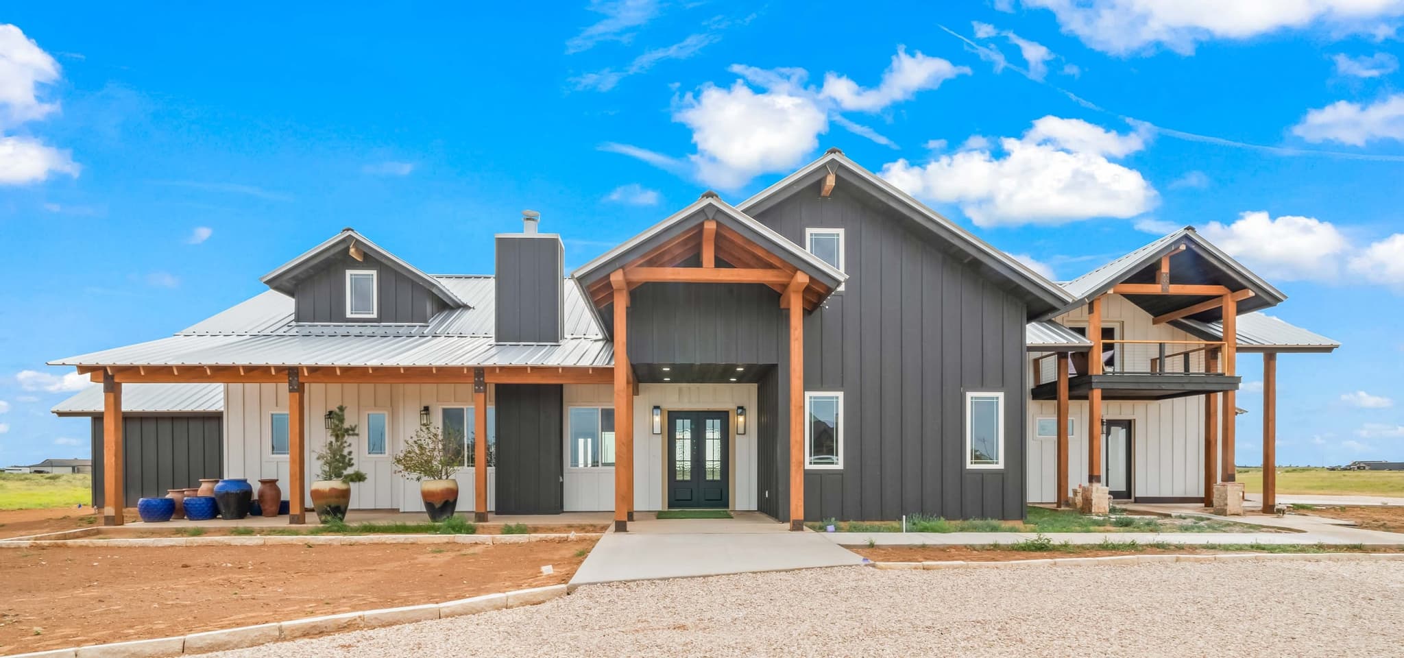 Lauderdale custom residence — black board-and-batten farmhouse with a metal panel roof and hewn-timber porch posts